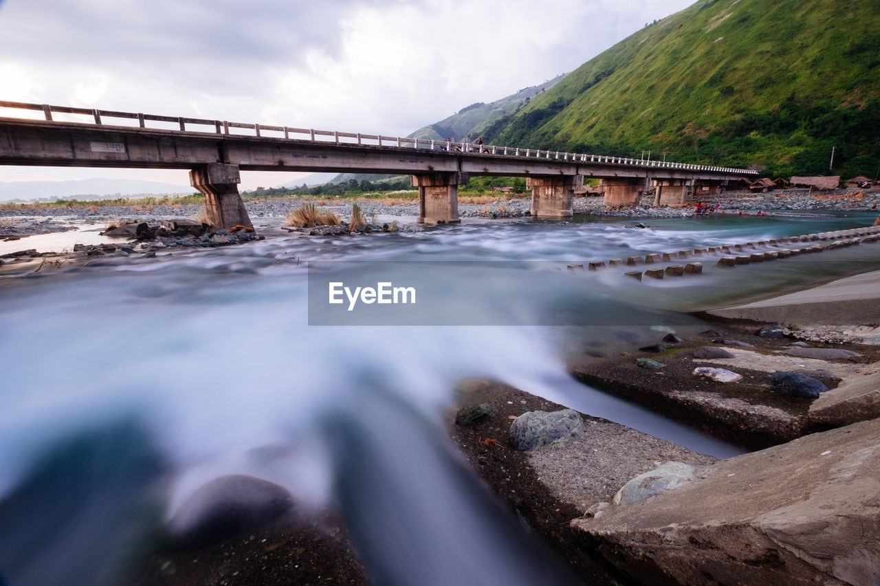 Blurred motion of river with bridge against sky