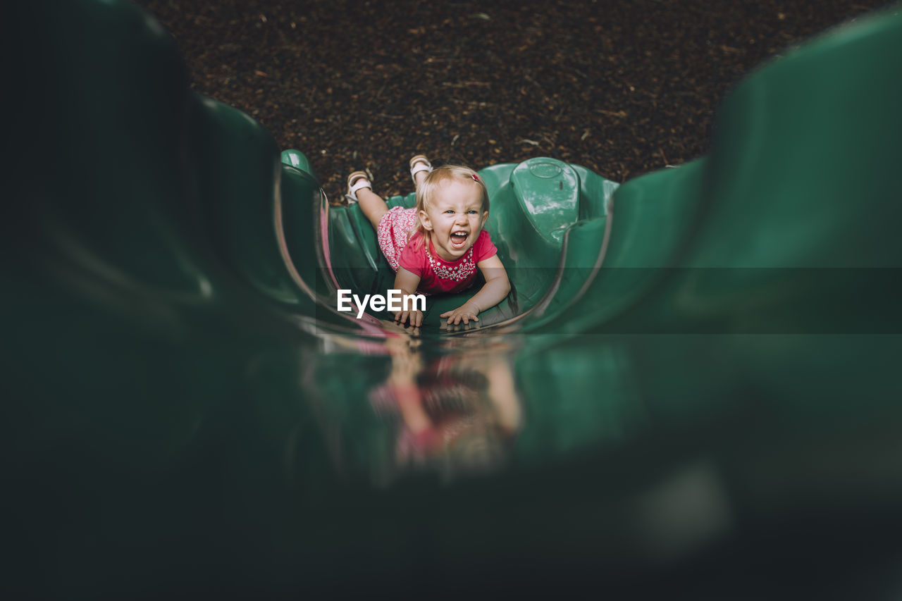 High angle portrait of happy baby girl playing on slide at playground