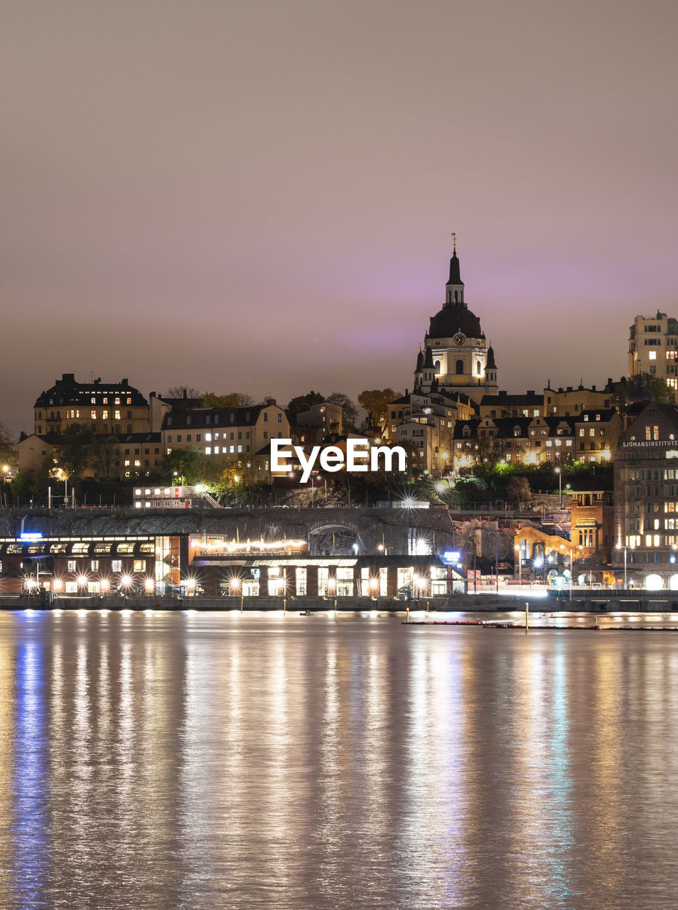 Cityscape view of södermalm stockholm during cloudy night with light reflections in the water.