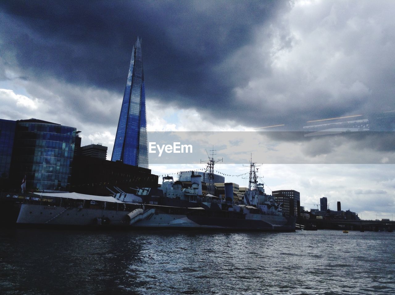 Ship moored on thames river by shard by against cloudy sky