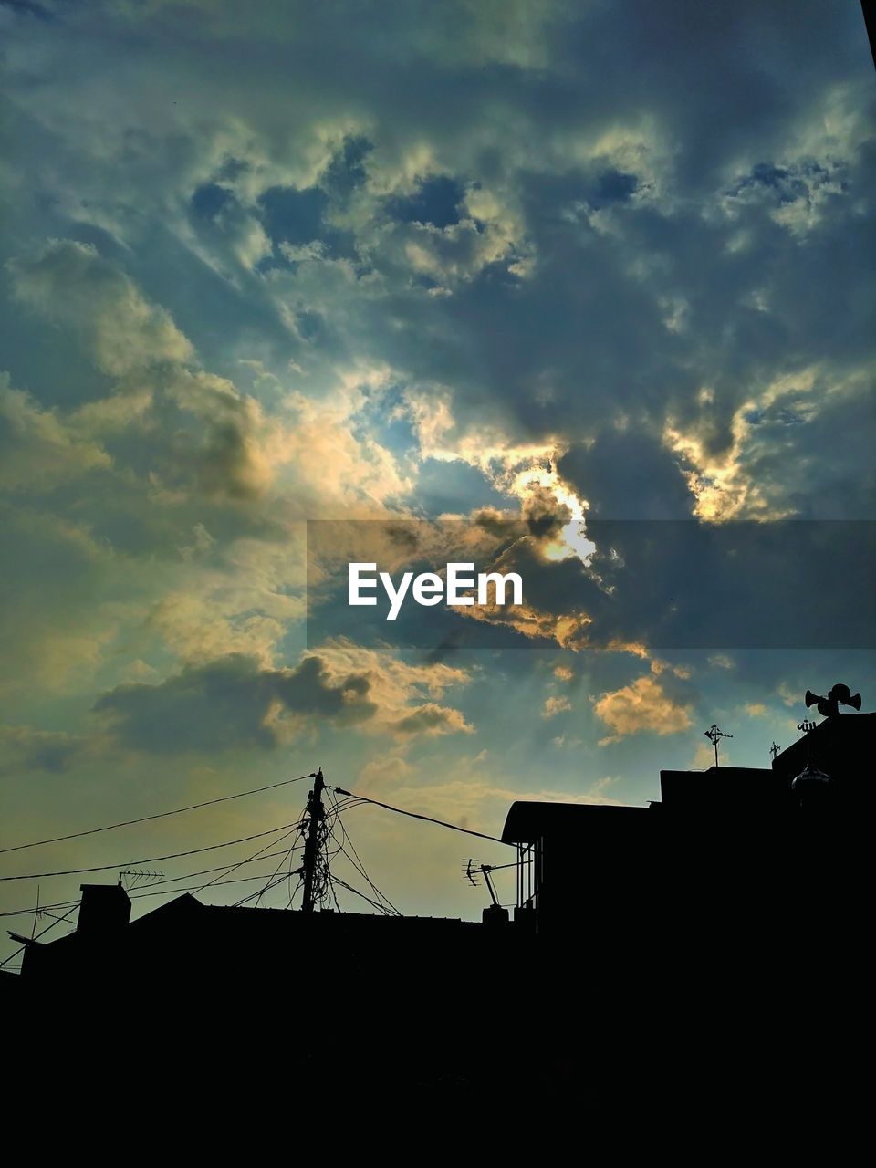 HIGH SECTION OF SILHOUETTE BUILDINGS AGAINST CLOUDS