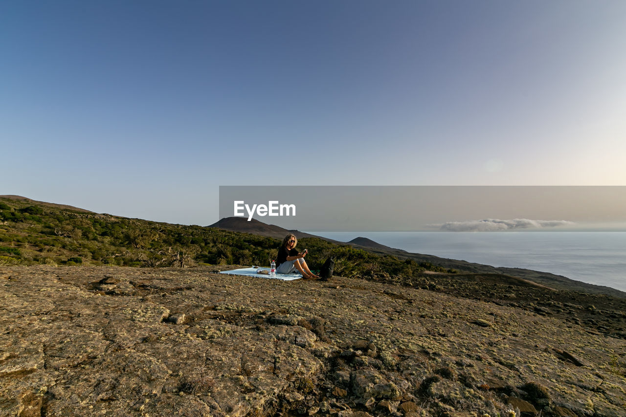 Woman on rock by sea against sky