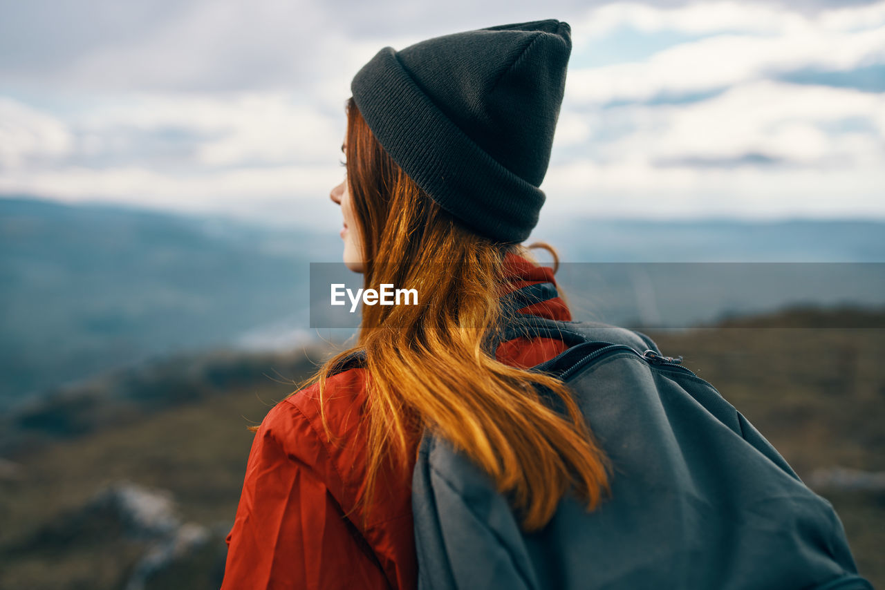 REAR VIEW OF WOMAN STANDING AGAINST MOUNTAIN