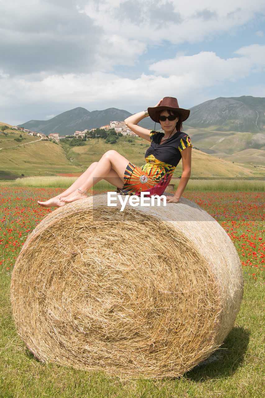 Portrait of woman wearing hat while sitting on hay bale