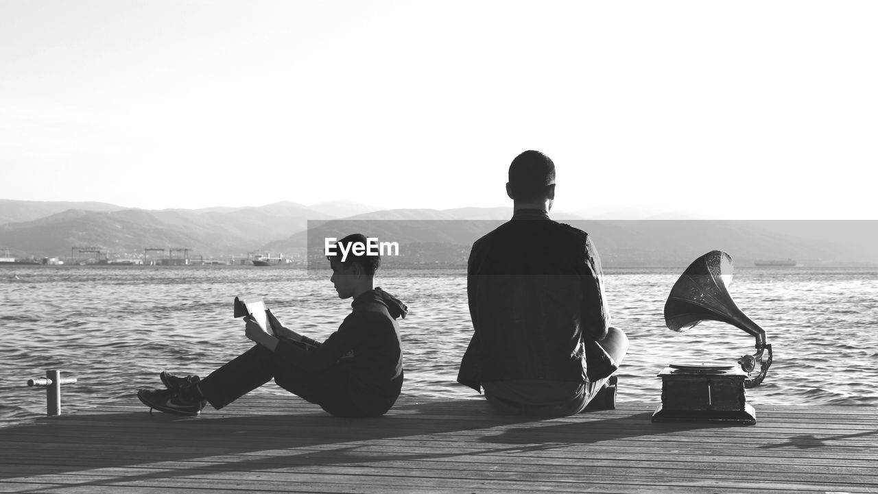 REAR VIEW OF COUPLE SITTING ON BEACH