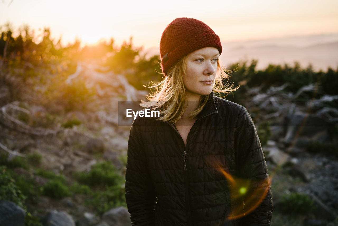 Woman looking away while standing on mountain against sky during sunset