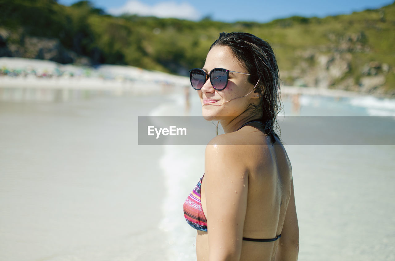 Side view of woman wearing sunglasses standing at beach