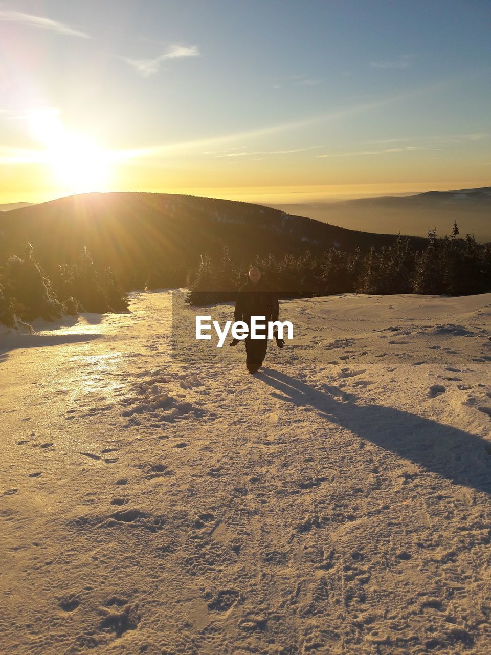 Full length of man on snow covered field against sky during sunset