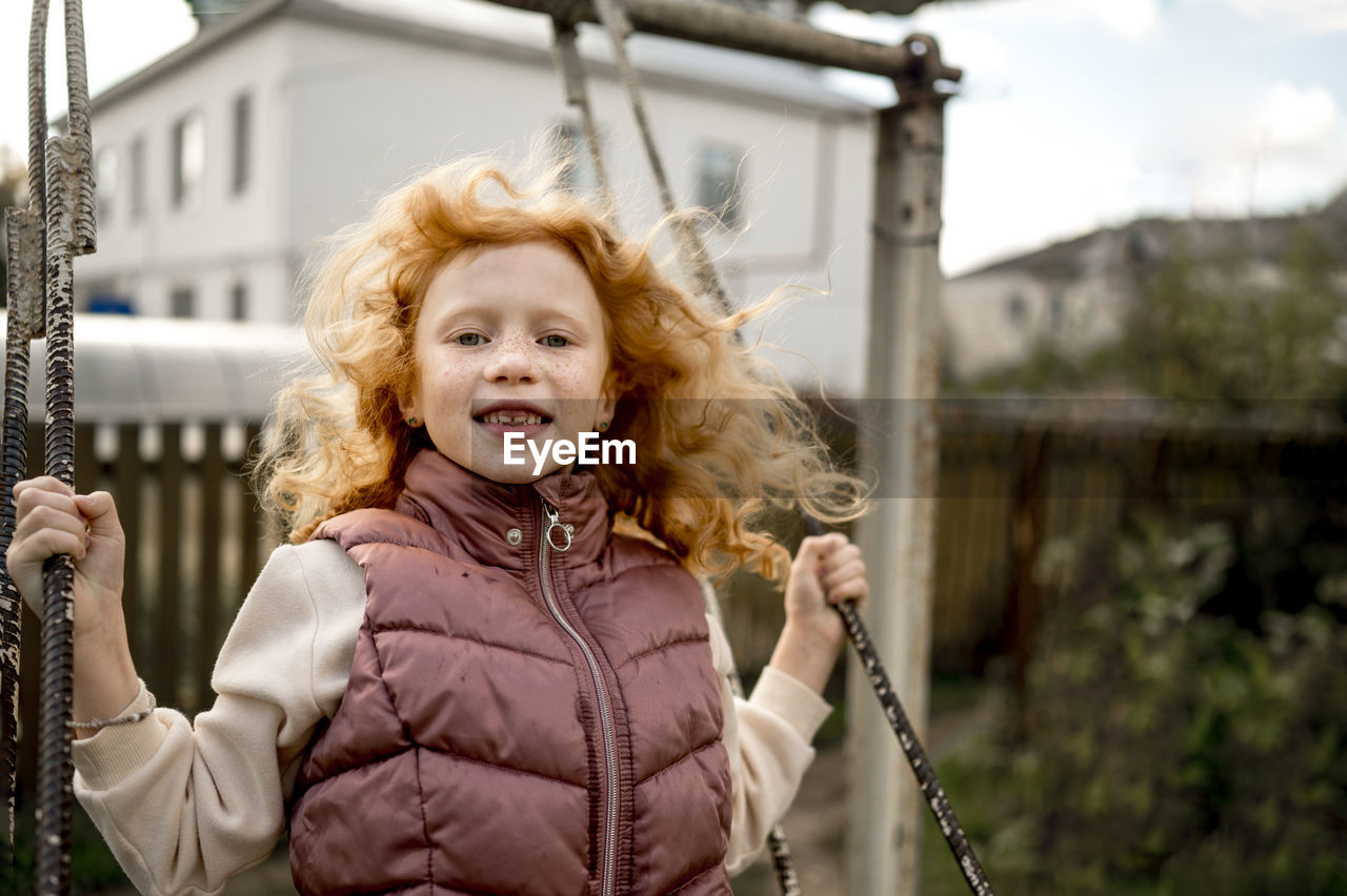 Smiling redhead girl swinging in garden