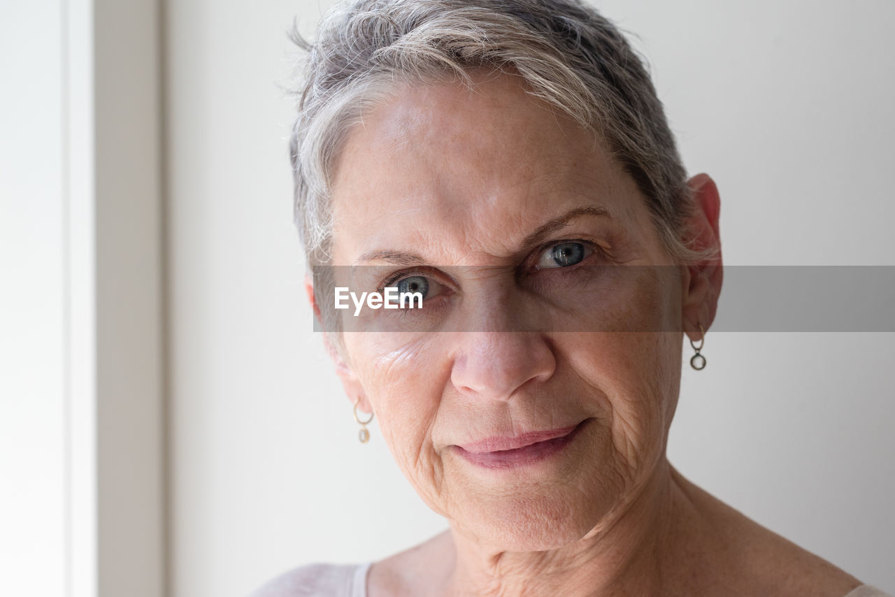 Close-up portrait of mature woman against wall at home