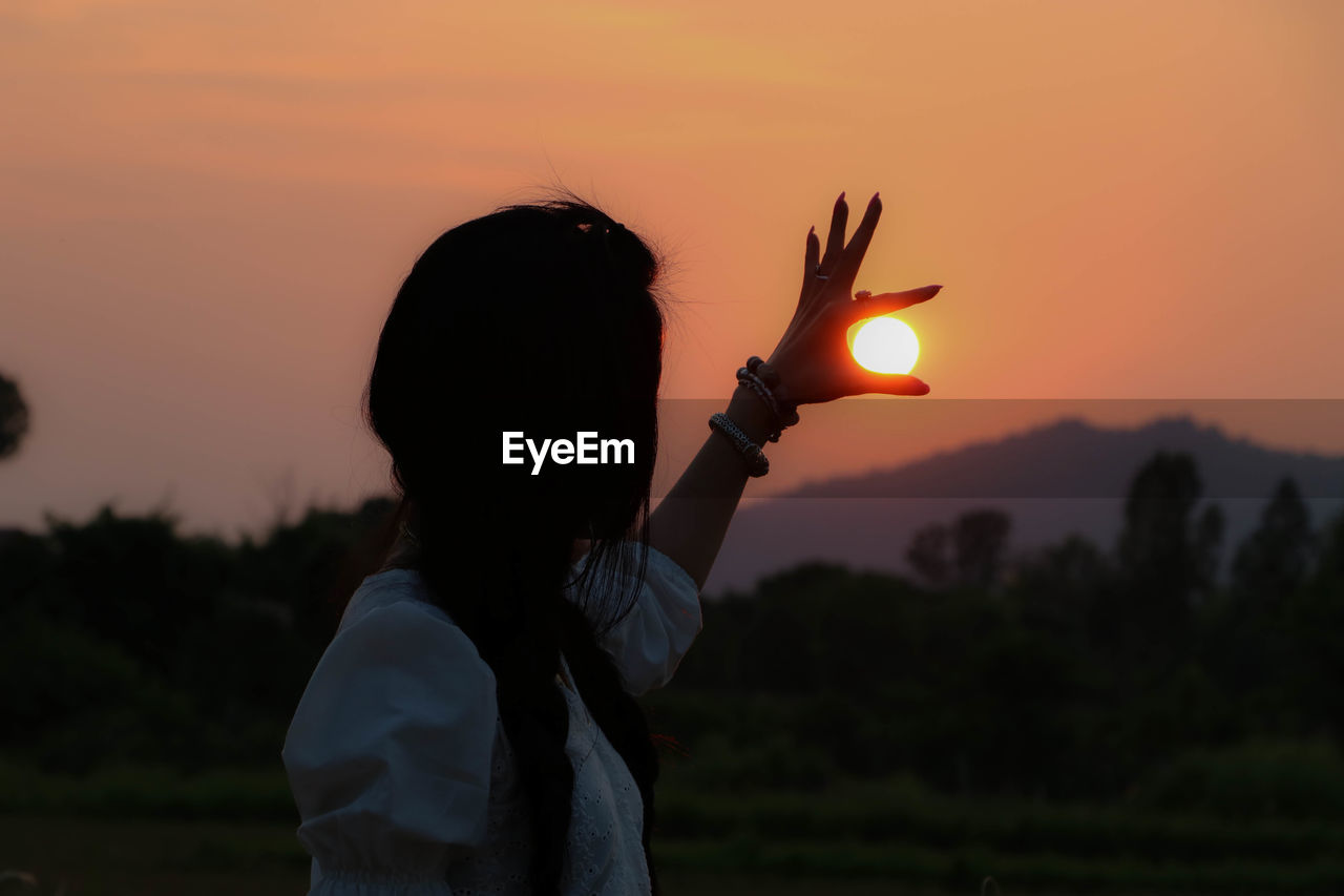 Woman gesturing against sky during sunset