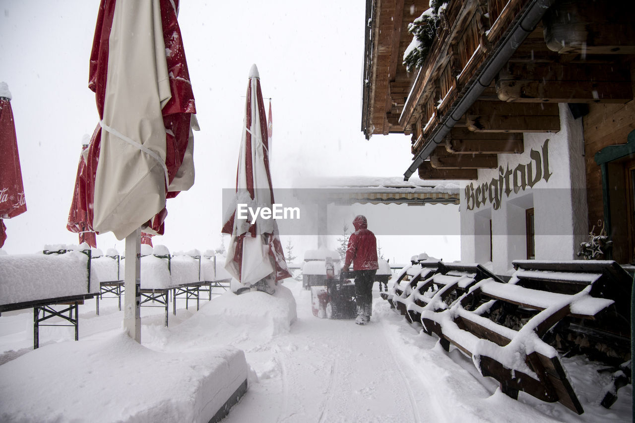 REAR VIEW OF PERSON STANDING ON SNOW COVERED BUILDINGS