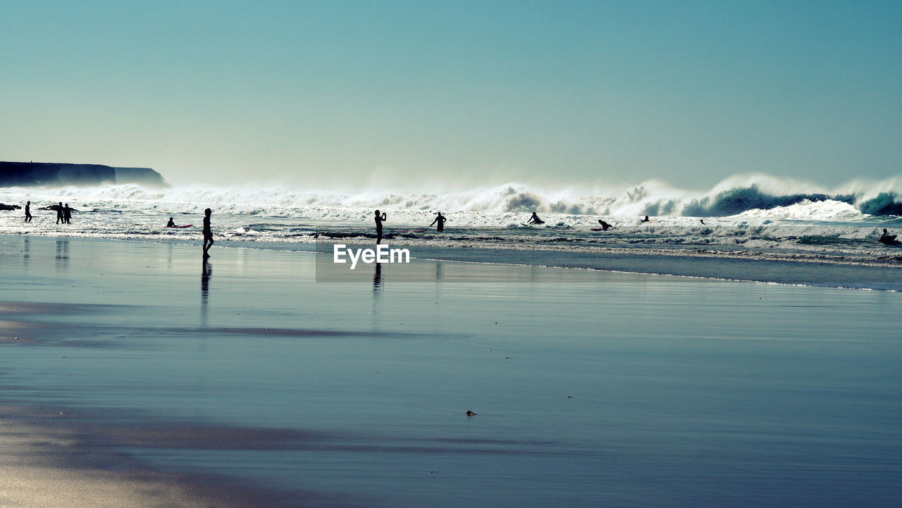 Surfers enjoying at beach against clear sky