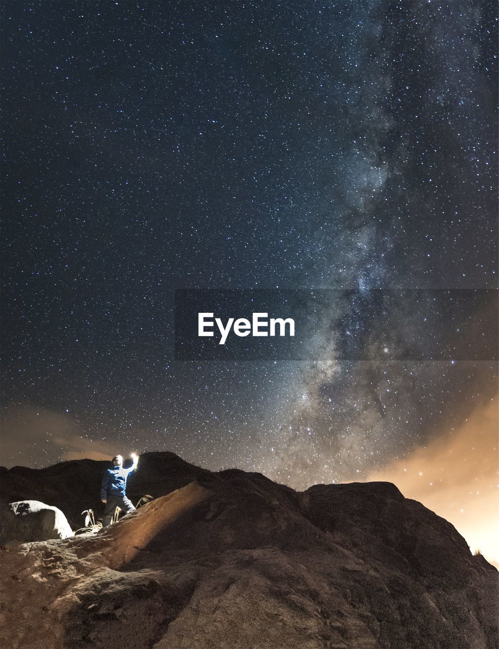 Man with illuminated lighting equipment on mountain against milky way