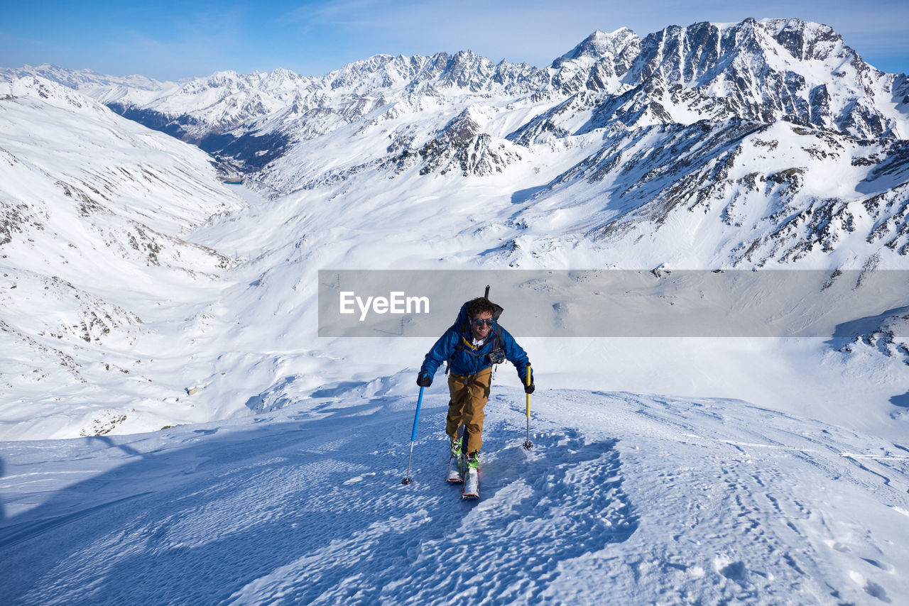 Man ski touring up slope with mountains behind him