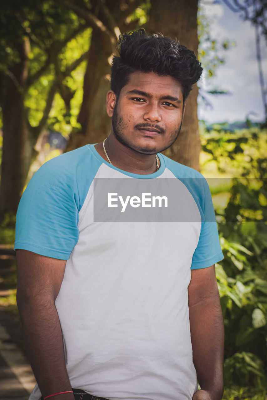 portrait of young man standing against tree