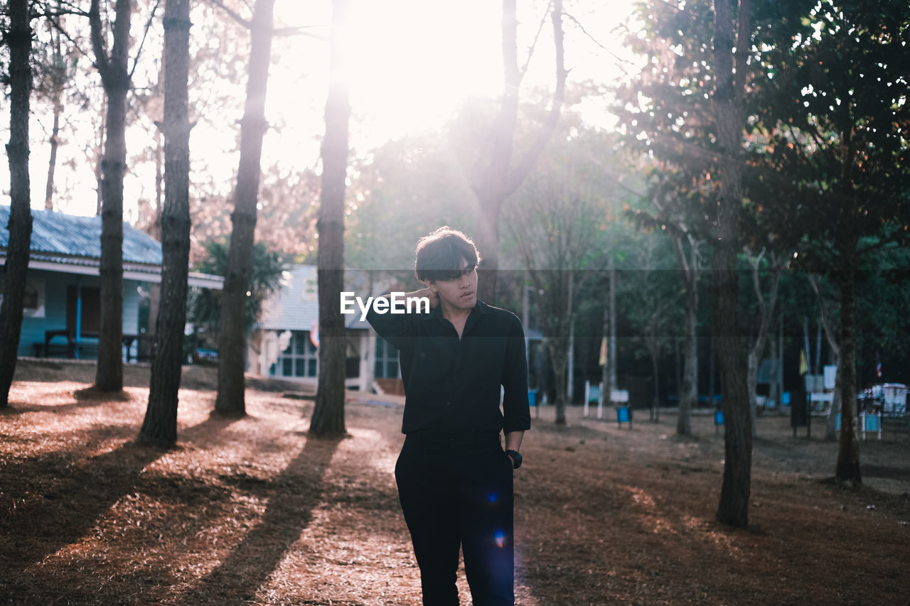 Young man standing against trees and houses on sunny day