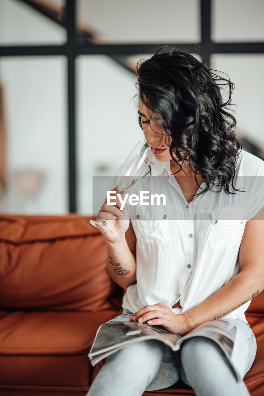 Businesswoman drinking champagne while reading magazine in office