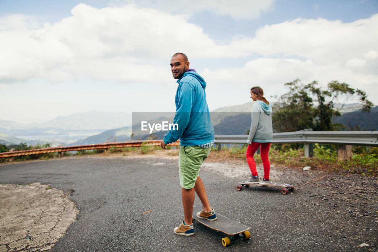 Couple skateboarding on road against sky