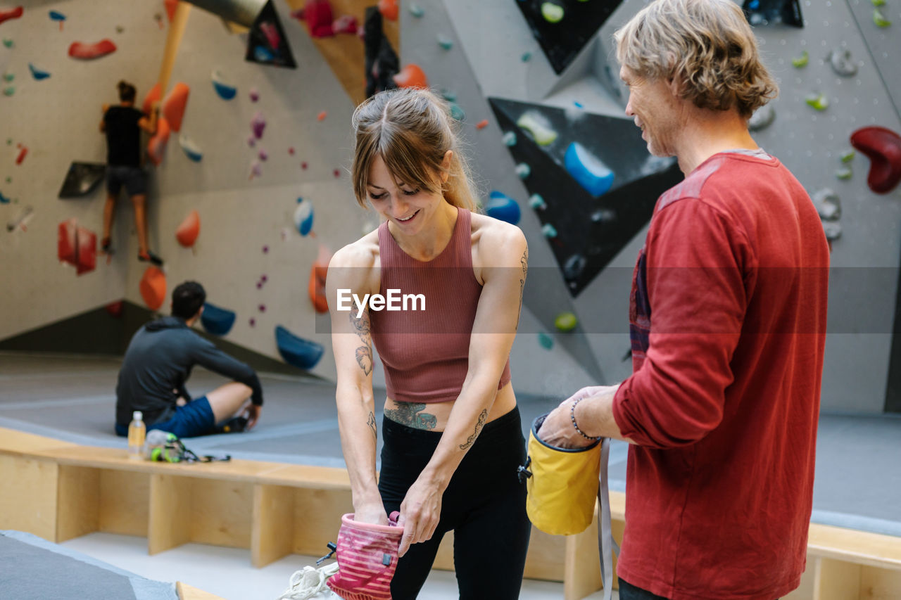 Mature instructor with smiling female student holding bag in gym