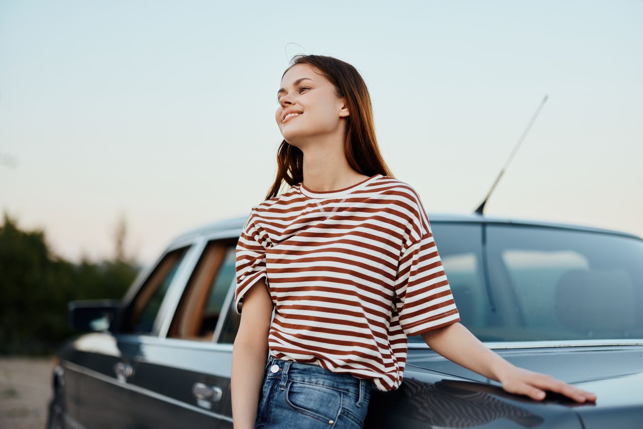 young woman sitting on car against sky