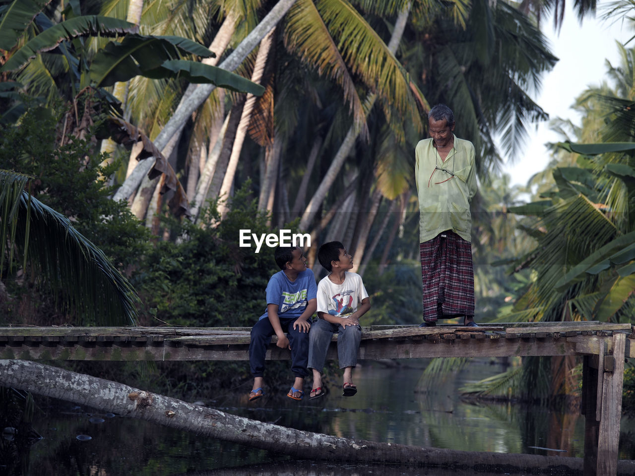 Man talking with boys sitting on footbridge over river