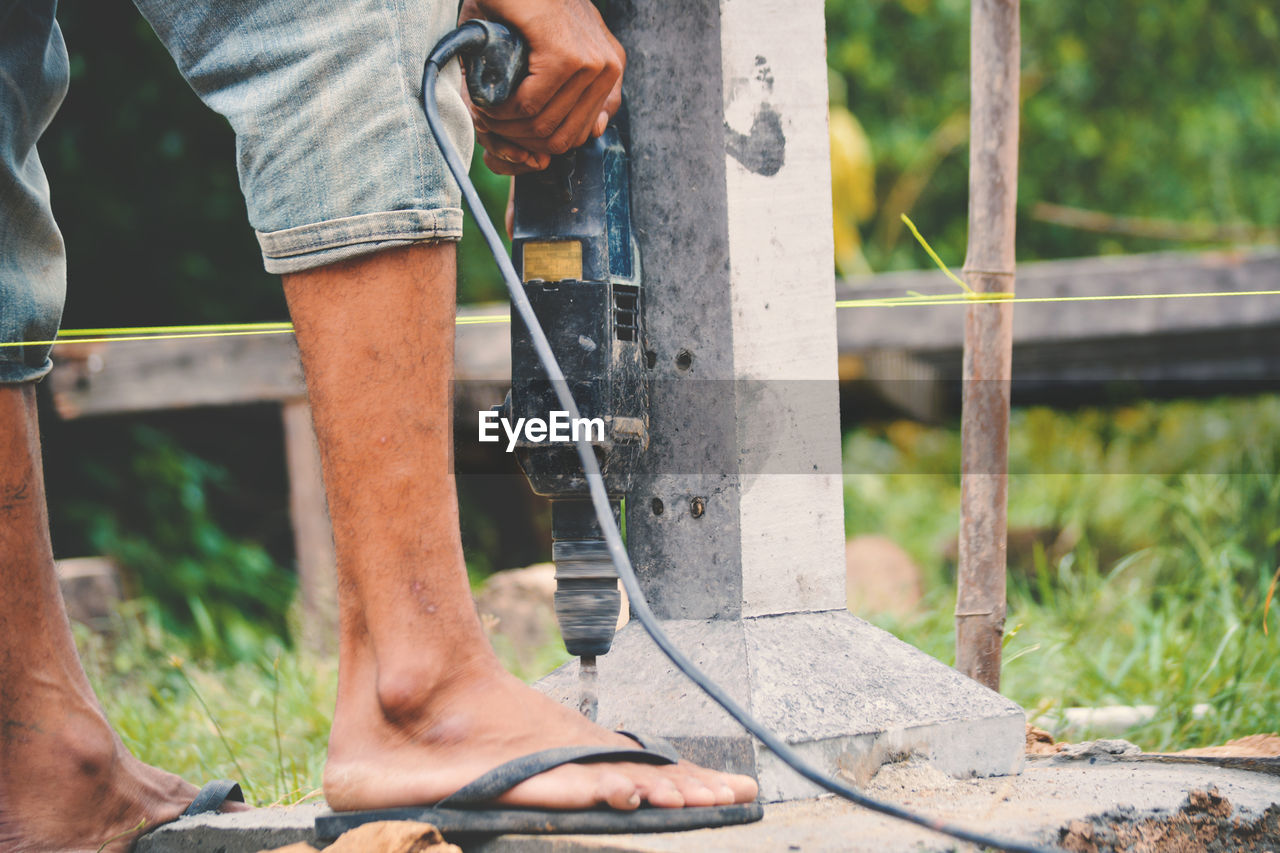 Low section of male worker drilling by column on field