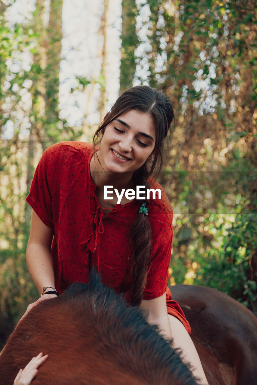 Smiling young woman sitting on horse in forest