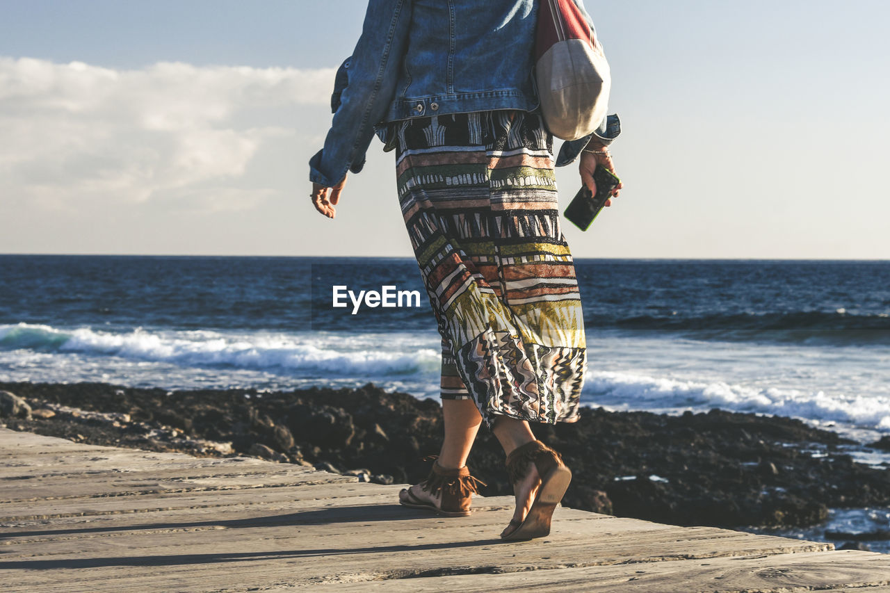 Low section of woman on pier over sea against sky