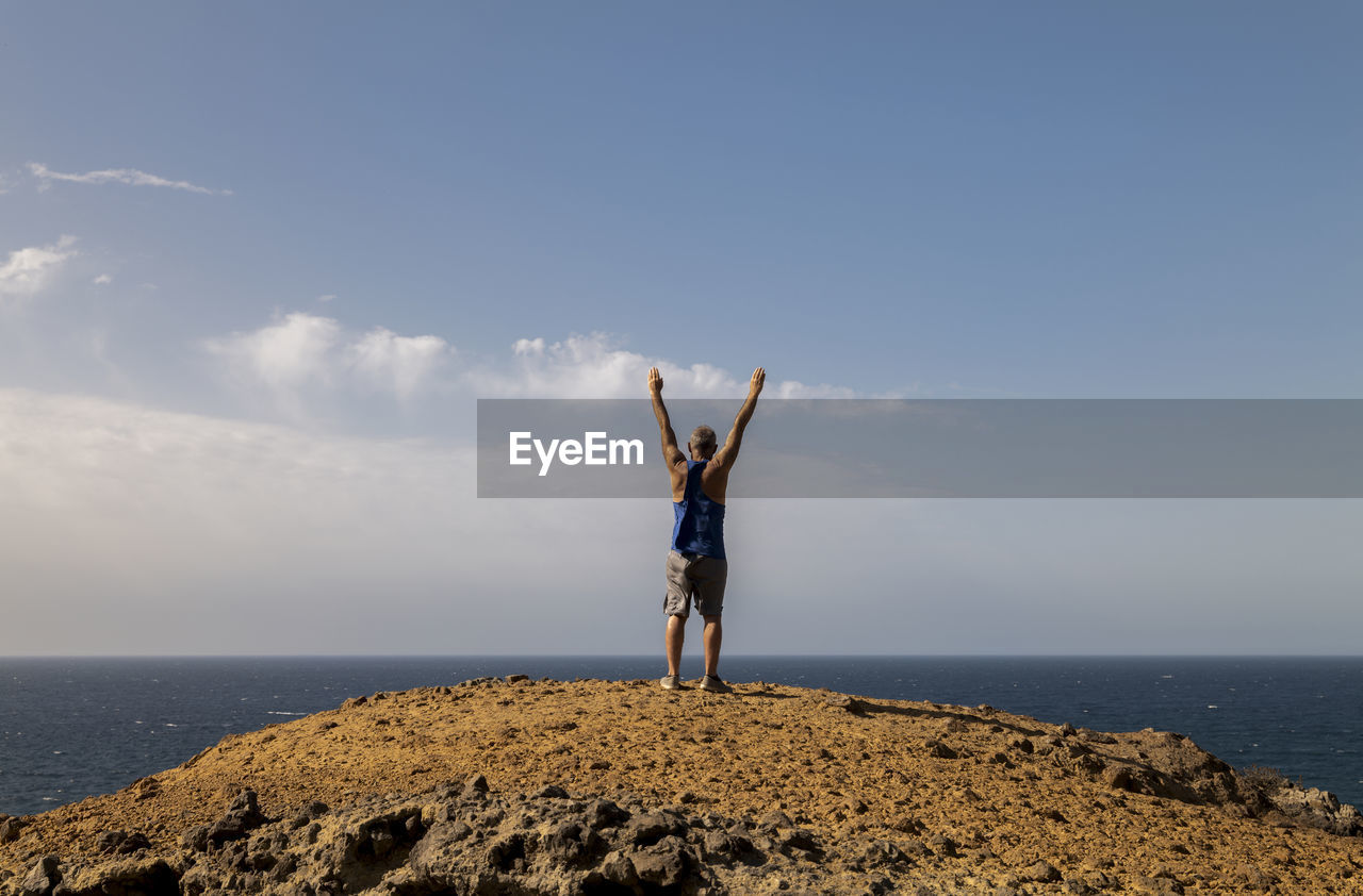 Man standing on rock by sea against sky