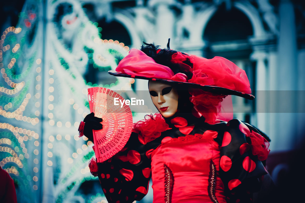 Woman with mask holding hand fan during carnival