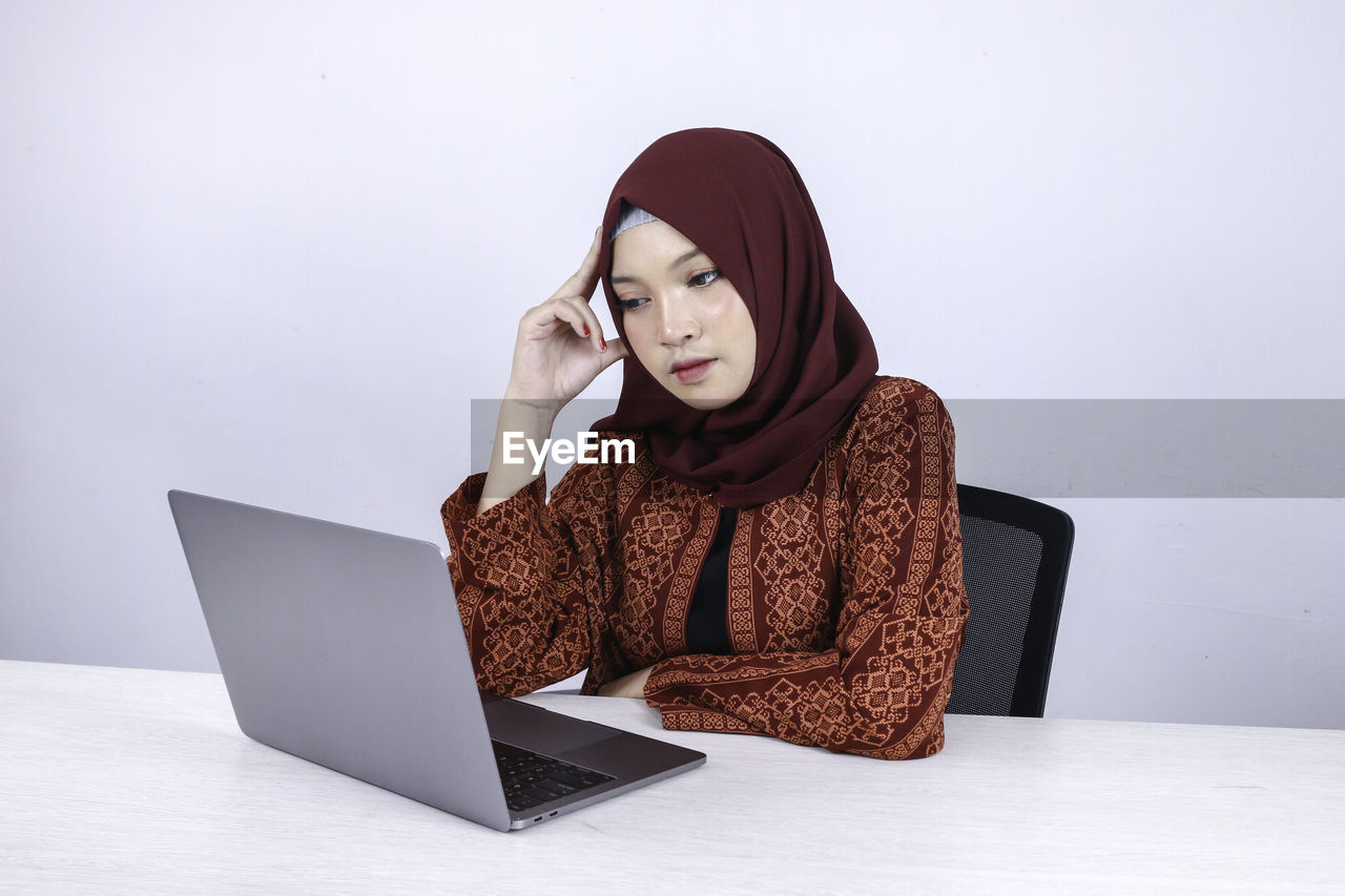 WOMAN LOOKING AT CAMERA WHILE SITTING ON TABLE