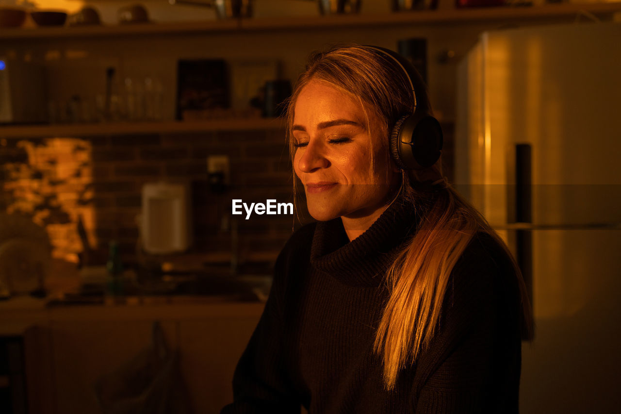 Woman listens to music with headphones in her ears in the kitchen. mobile phone, technology.