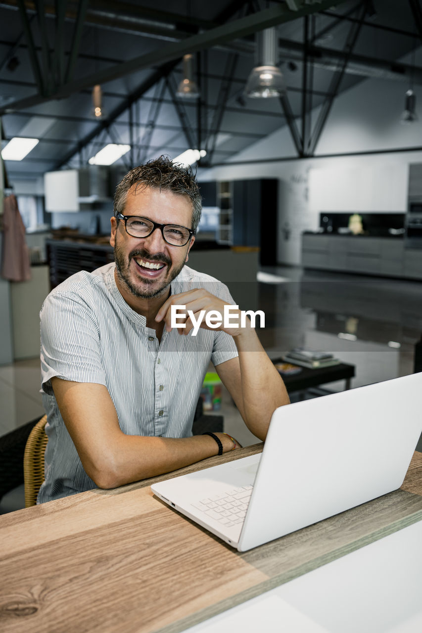 Cheerful handsome male freelancer sitting with laptop at desk while working in office