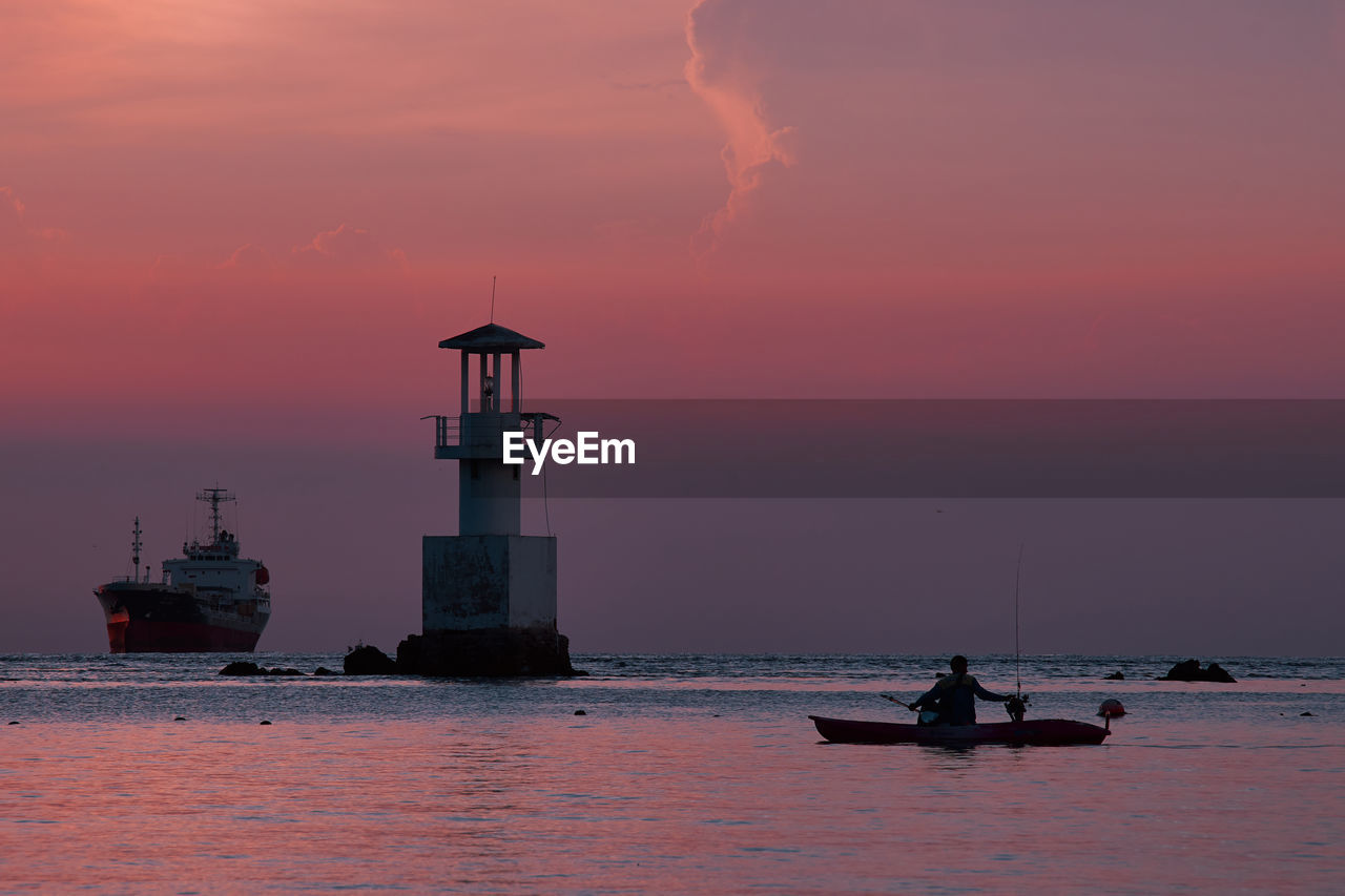 Silhouette lighthouse on sea against sky during sunset