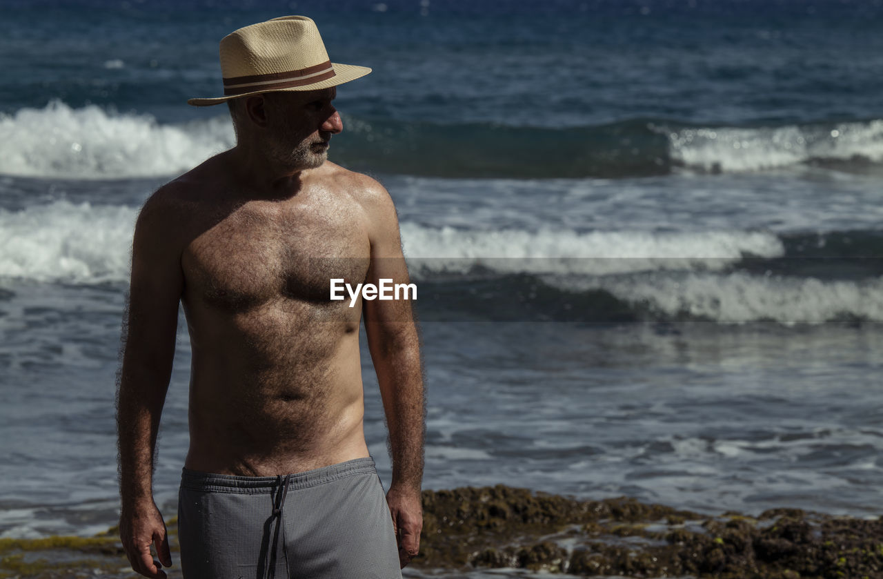 Portrait of shirtless man in hat against sea