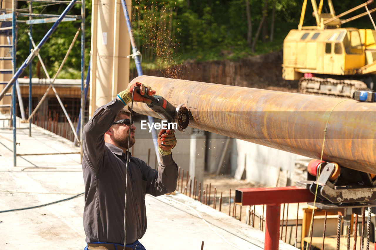 Worker cutting metal with electric saw against trees