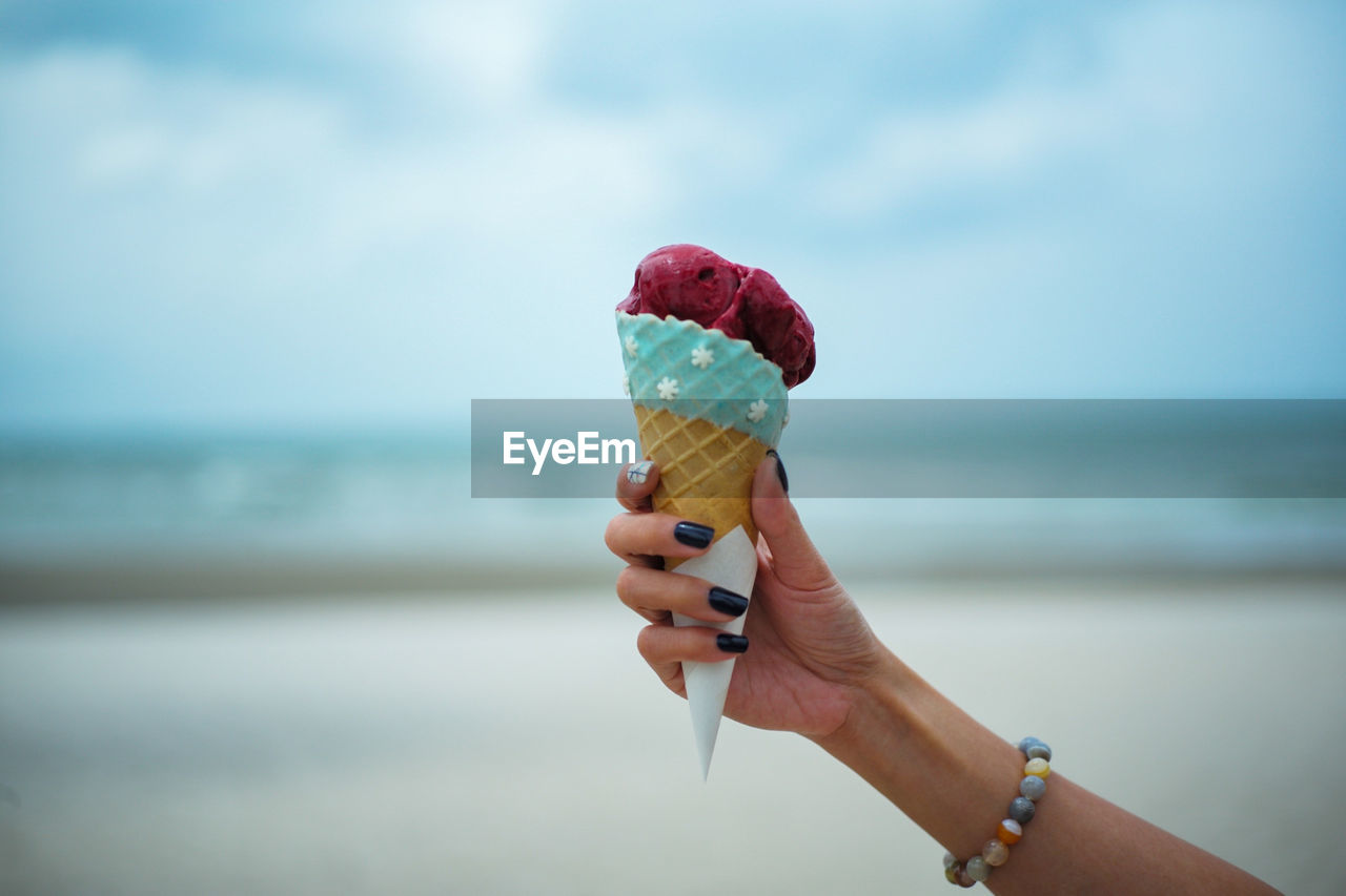 Cropped hand of woman having ice cream cone at beach