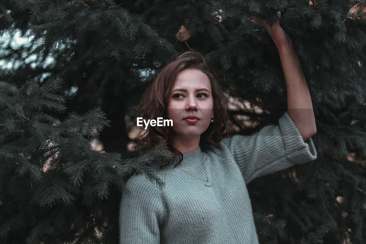 Young woman looking away while standing against trees in park