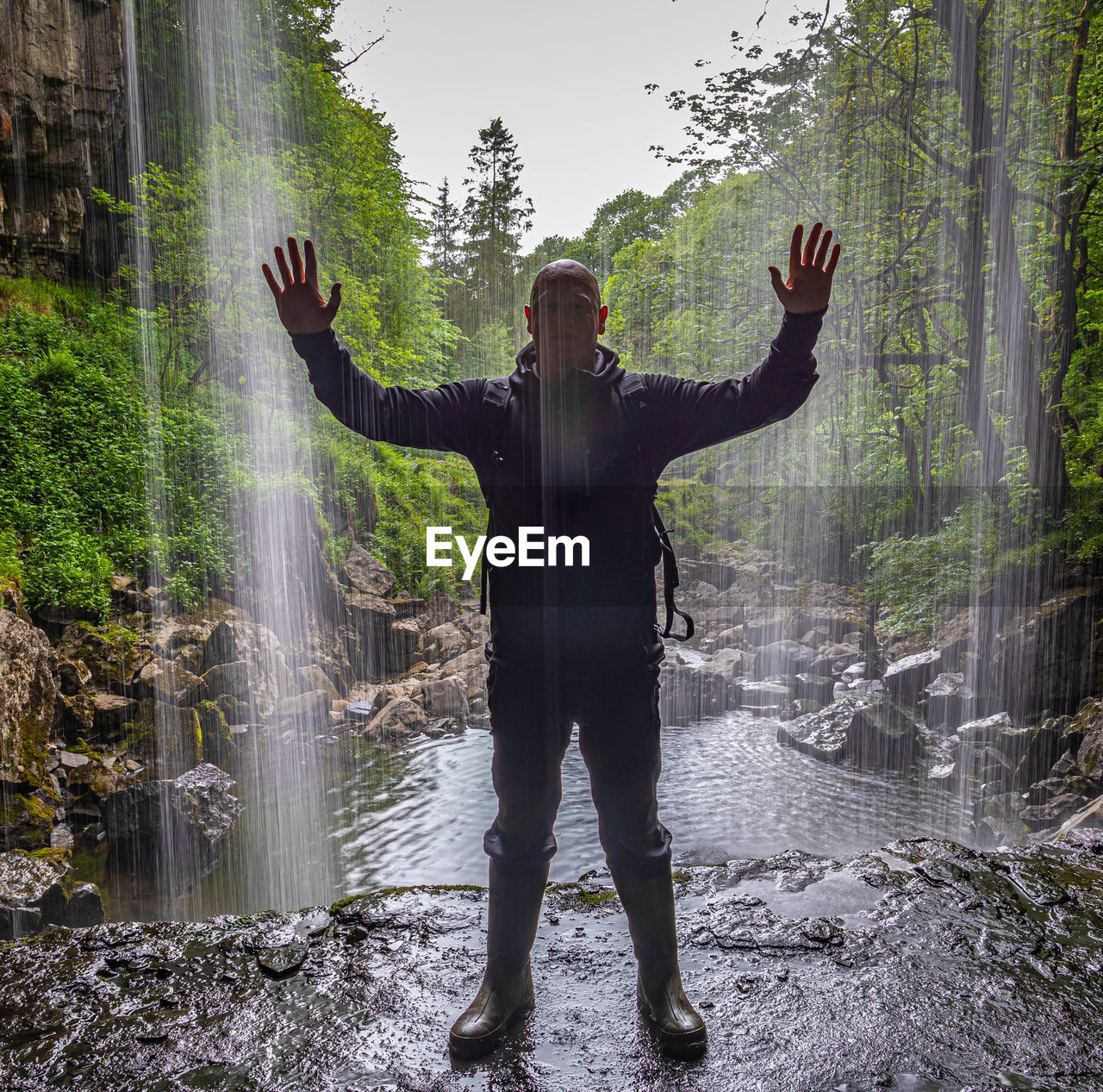 FULL LENGTH OF MAN WITH ARMS OUTSTRETCHED STANDING BY PLANTS IN FOREST