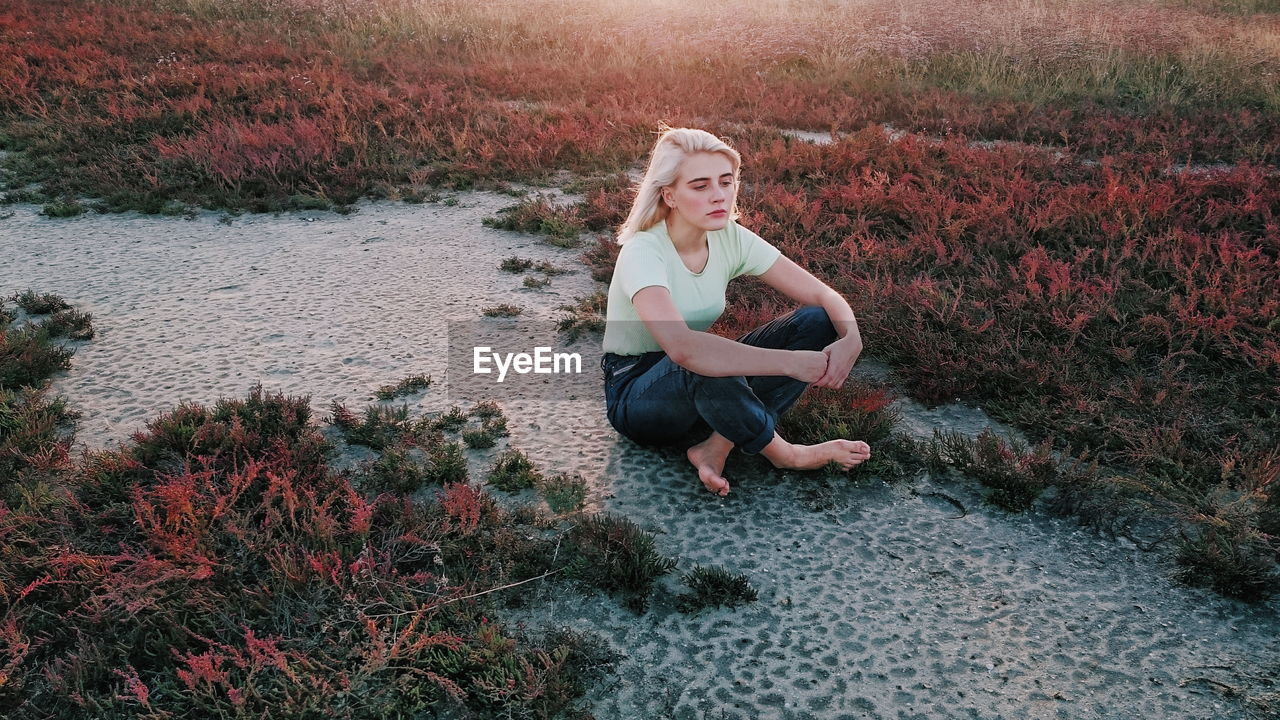 Young woman with cross-legged sitting by grass on field