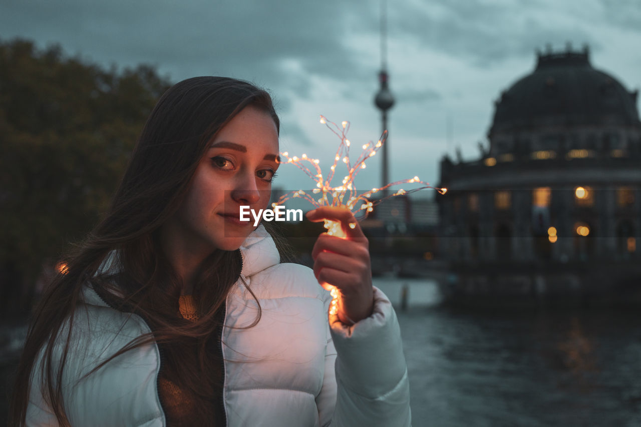 Portrait of young woman holding illuminated lights with fernsehturm in background