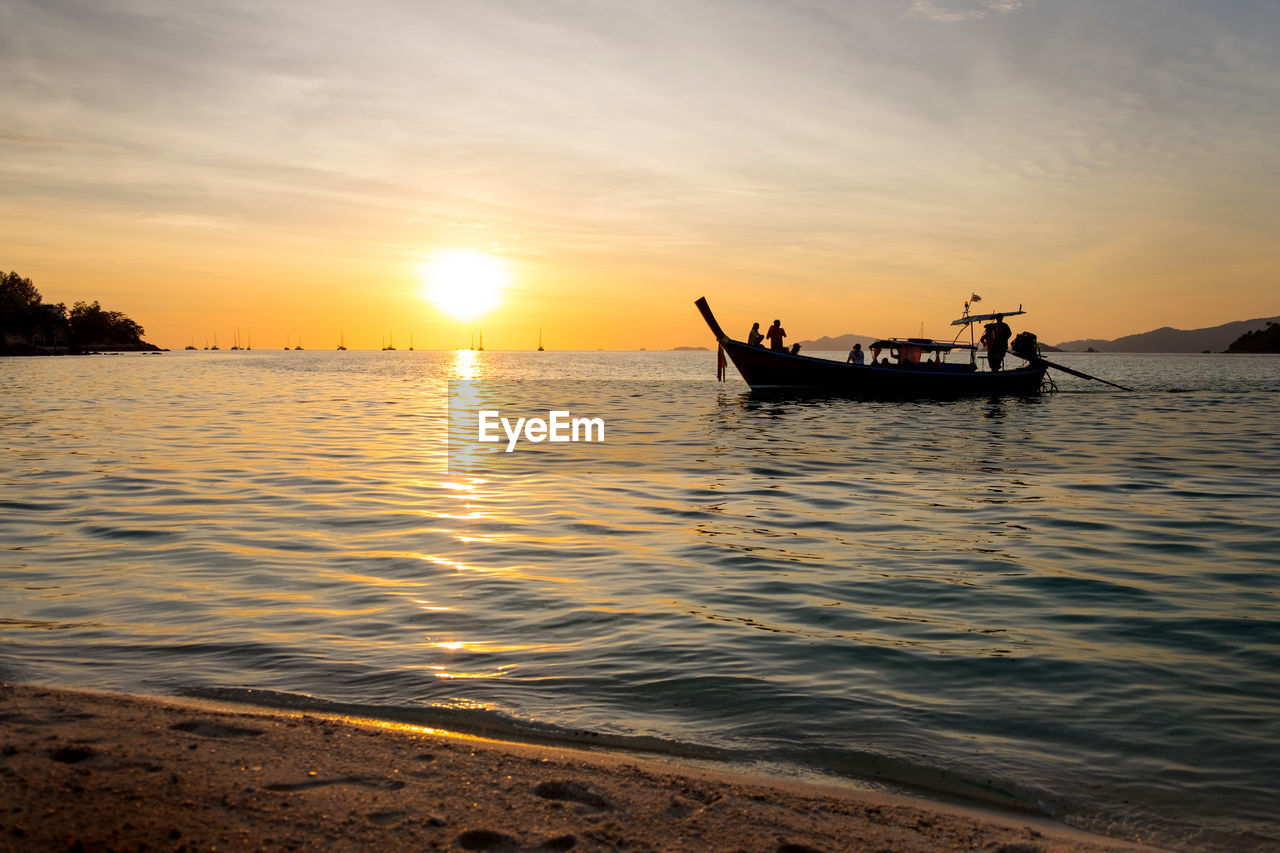 Silhouette people on longtail boat in sea during sunset