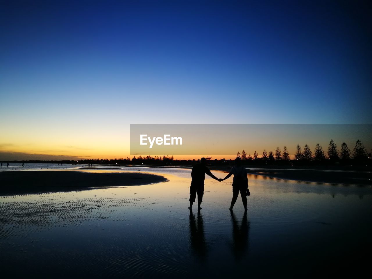 Silhouette couple holding hands at beach against during sunset