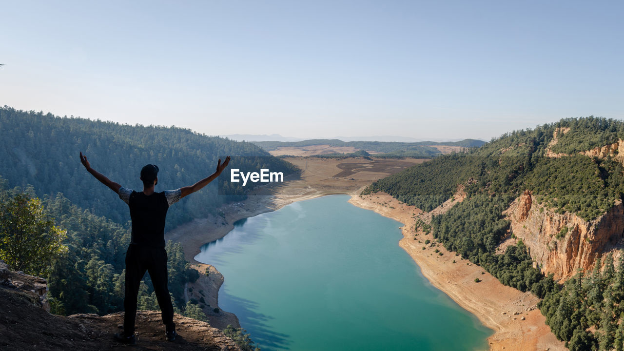 REAR VIEW OF MAN LOOKING AT VIEW OF MOUNTAINS