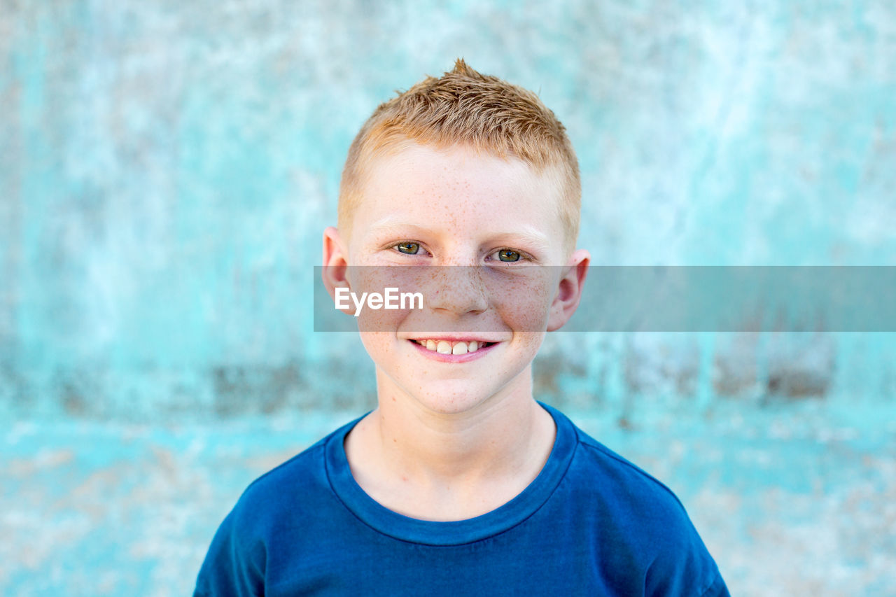 Portrait of a red head boy with freckles with a blue background