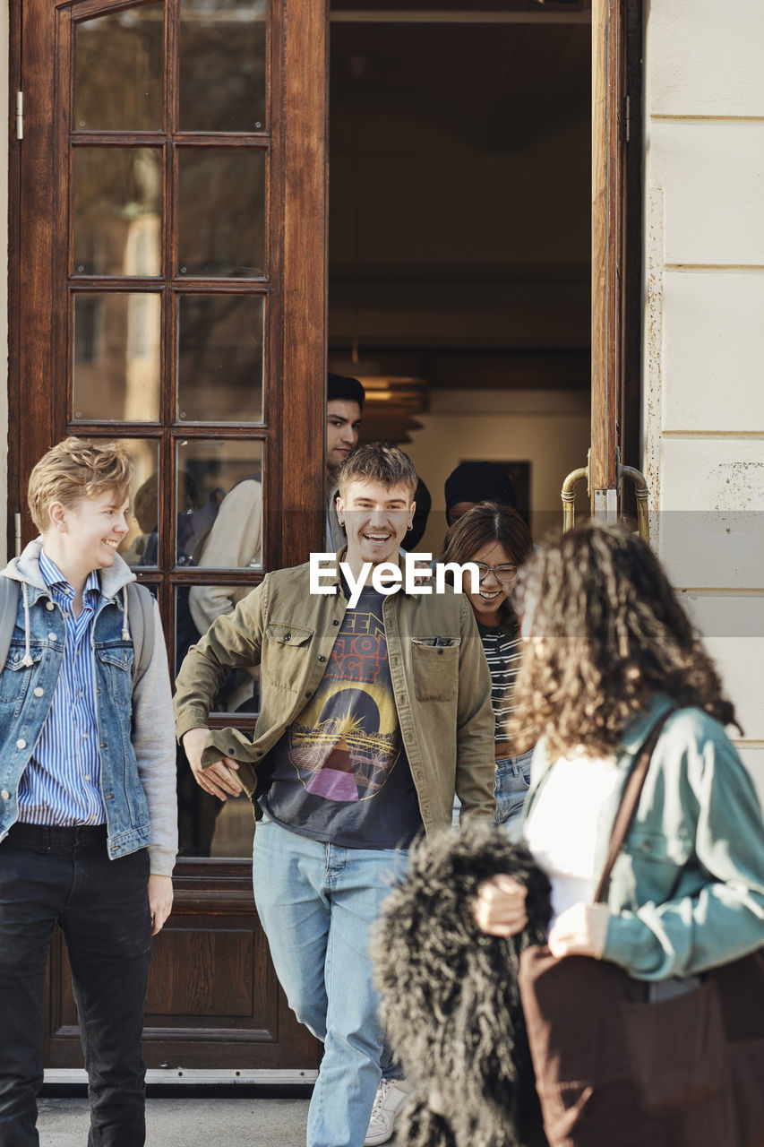 Happy male and female students walking out through university door