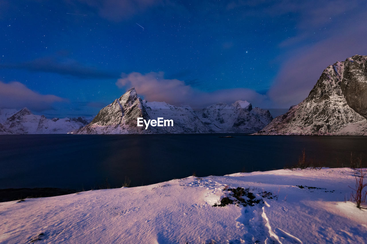 Scenic view of lake by snowcapped mountains against sky at night