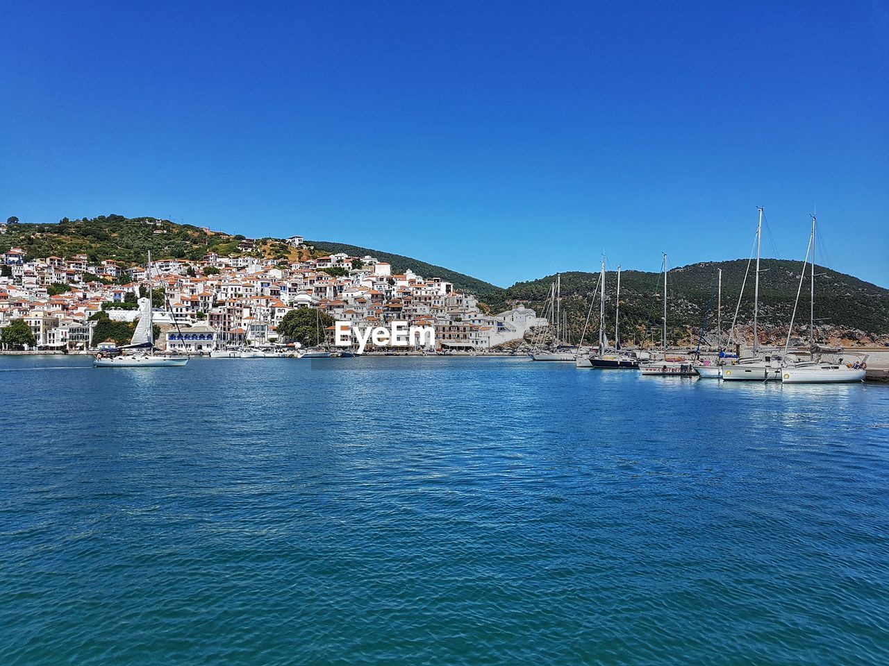 SAILBOATS MOORED IN SEA AGAINST BLUE SKY