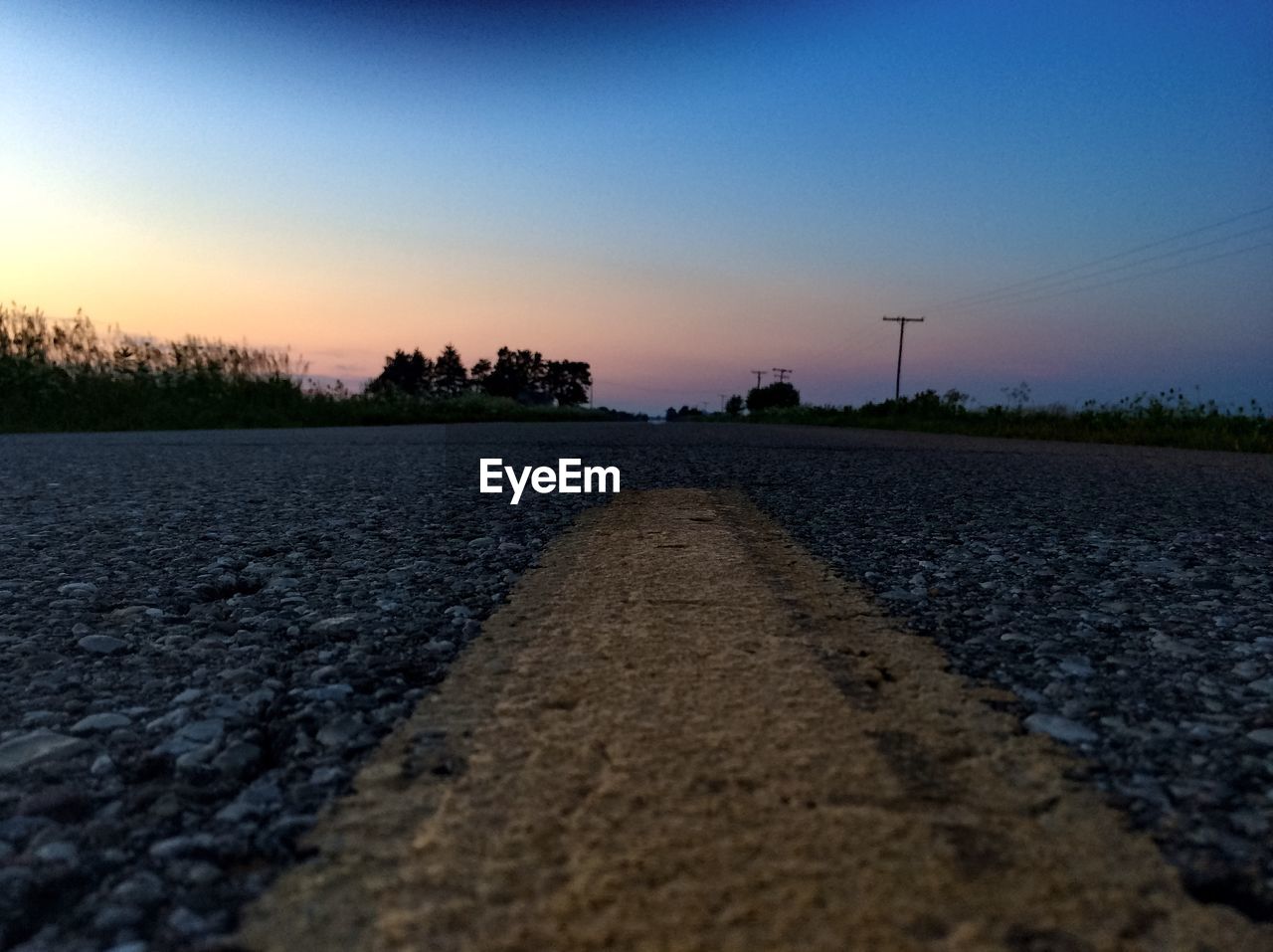 Surface level of empty road against clear sky during sunset
